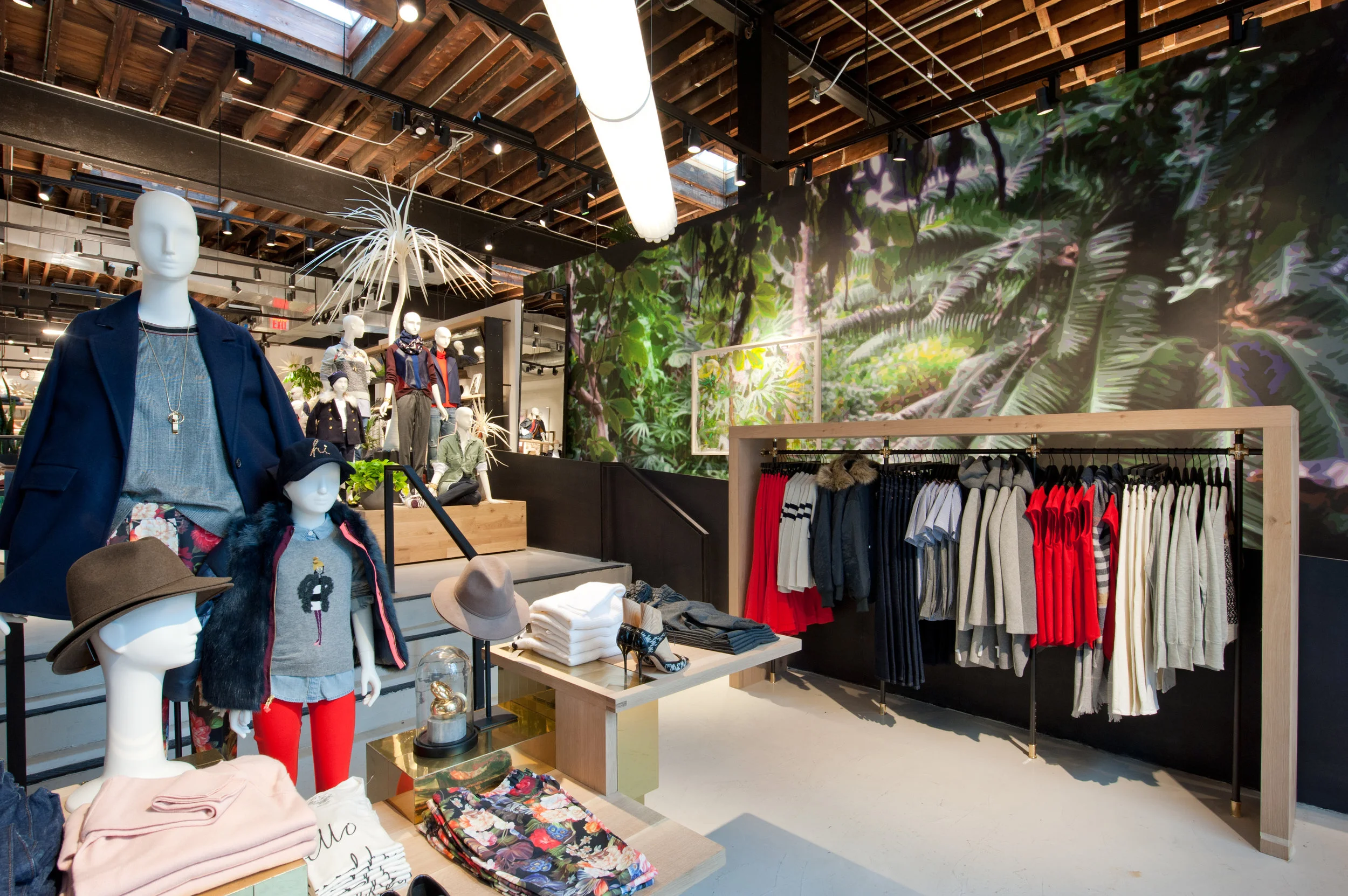 Mannequins of a woman and child to the left of a display rack holding women's clothes in front of a leafy green wallpaper in J Crew Williamsburg. MEP designed by 2L Engineering.