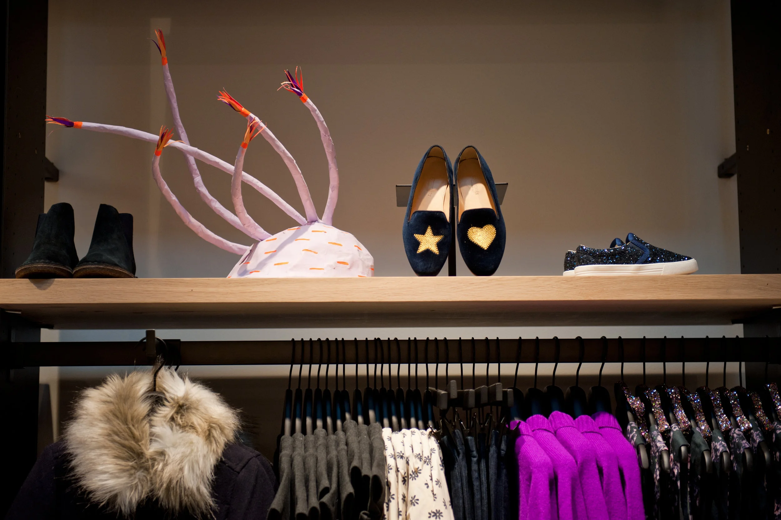 Loafers with a gold star and heart, sneakers, and booties beside a whimsical display over a clothing rack holding kid's outfits. MEP designed by 2L Engineering.