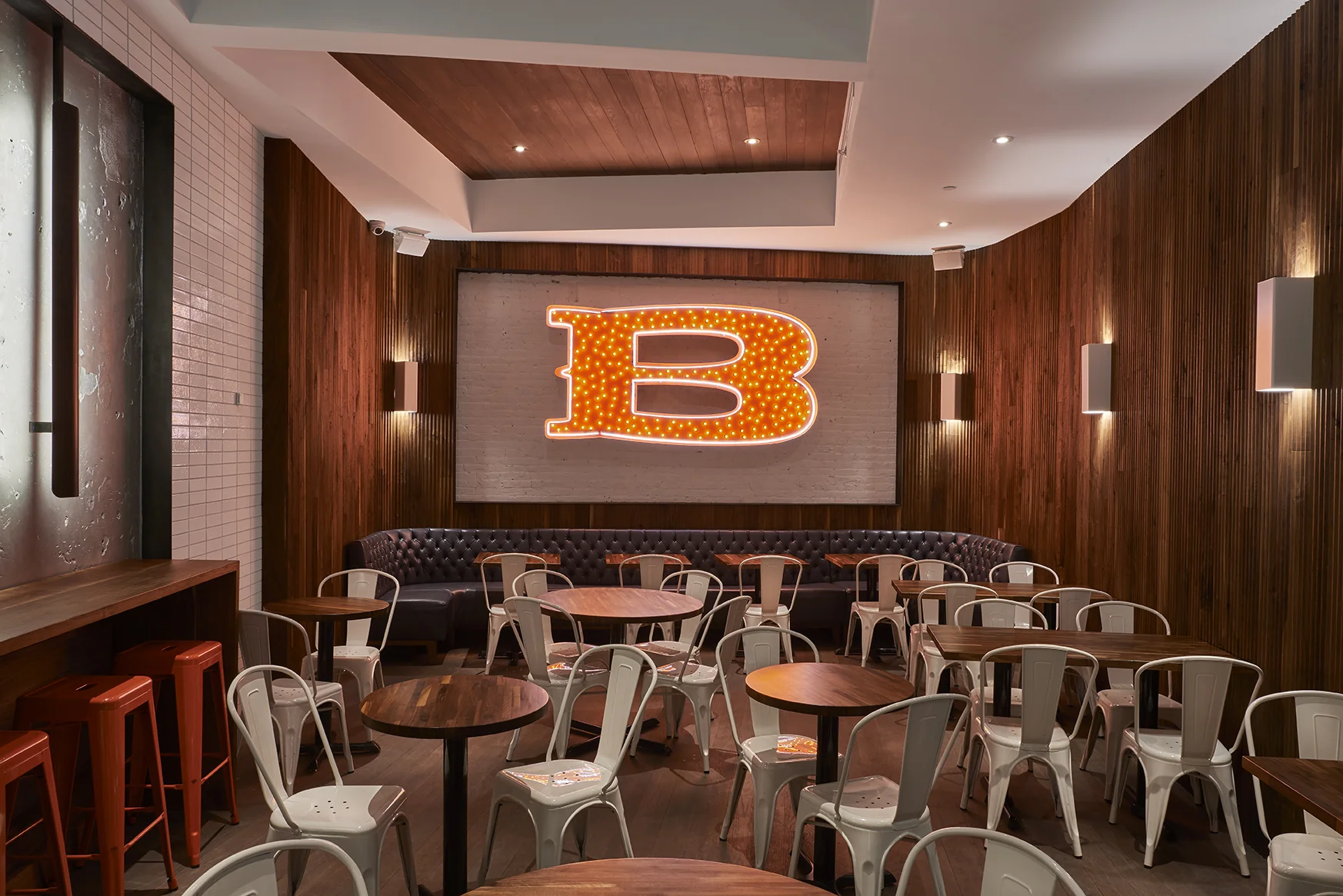 Large illuminated red B with yellow lights mounted on a white brick wall and surrounded by wooden lining over a seating area for customers at Baked Tribeca. MEP by 2L Engineering.
