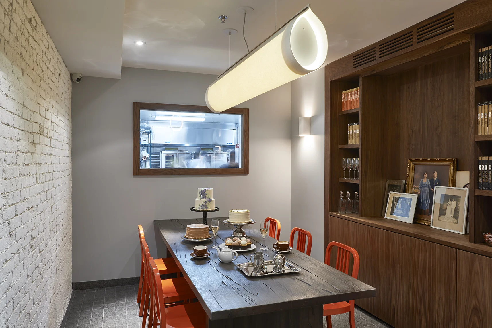 Private dining space in Baked Tribeca, with champagne, cakes, and pastries on the wooden table and a view into the kitchen. MEP provided by 2L Engineering.