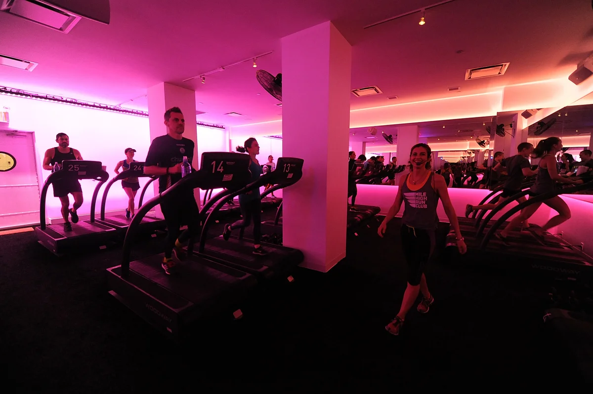 Fitness instructor leading a class as people run on various treadmills in a pink lit studio at the Mile High Run Club in New York, with MEP designed by 2L Engineering.