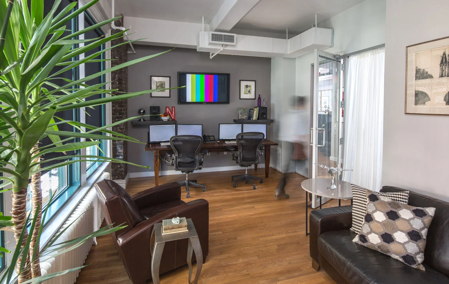 Man leaving an office space with lounge area and multiple monitors, including one showing vertical color bars in the studio of Napoleon. MEP designed by 2L Engineering.