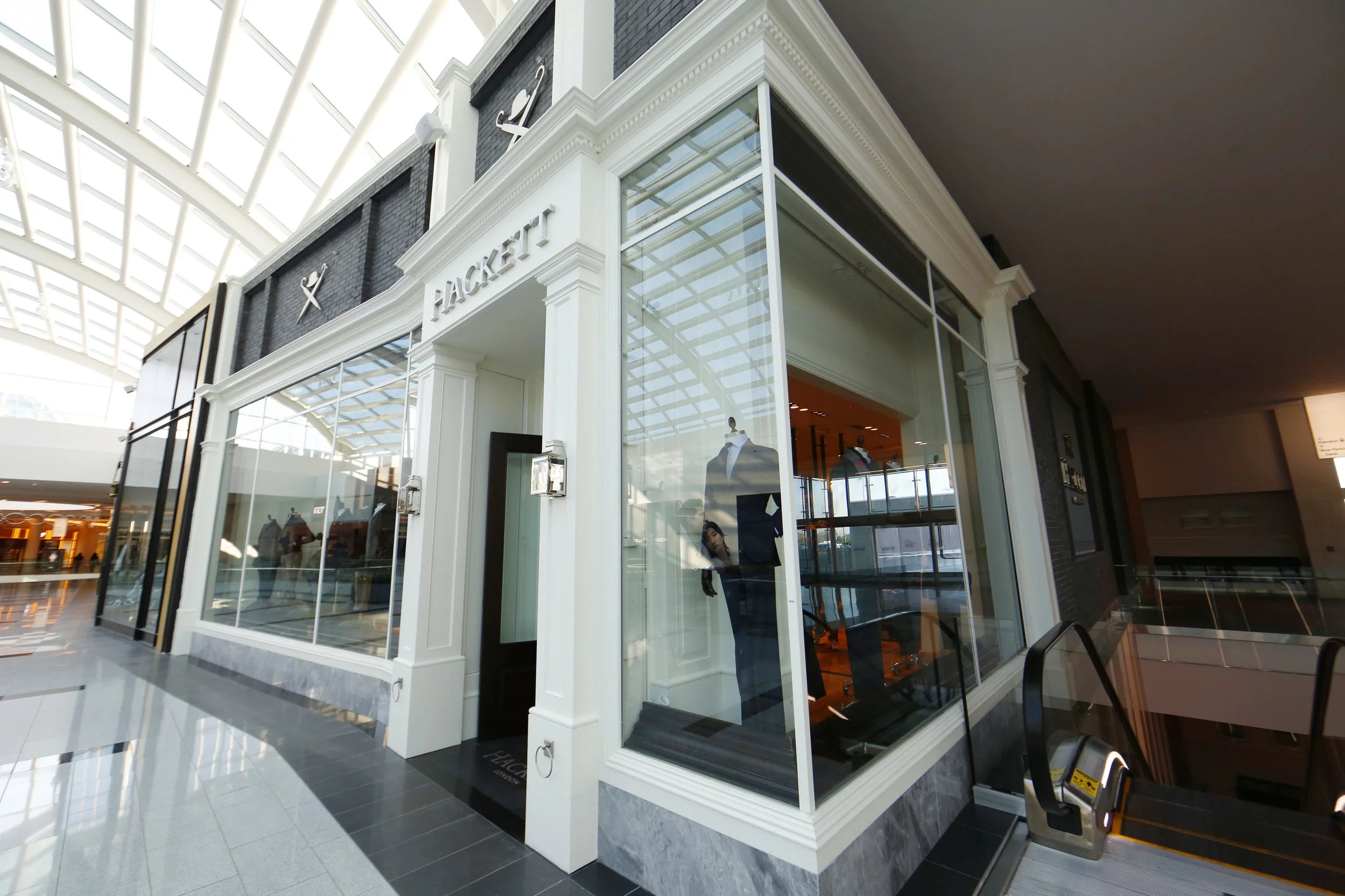 Window display showcasing mannequins wearing suits in Hackett London's retail store in the Woodbury Common Premium Outlet. MEP design services by 2L Engineering.