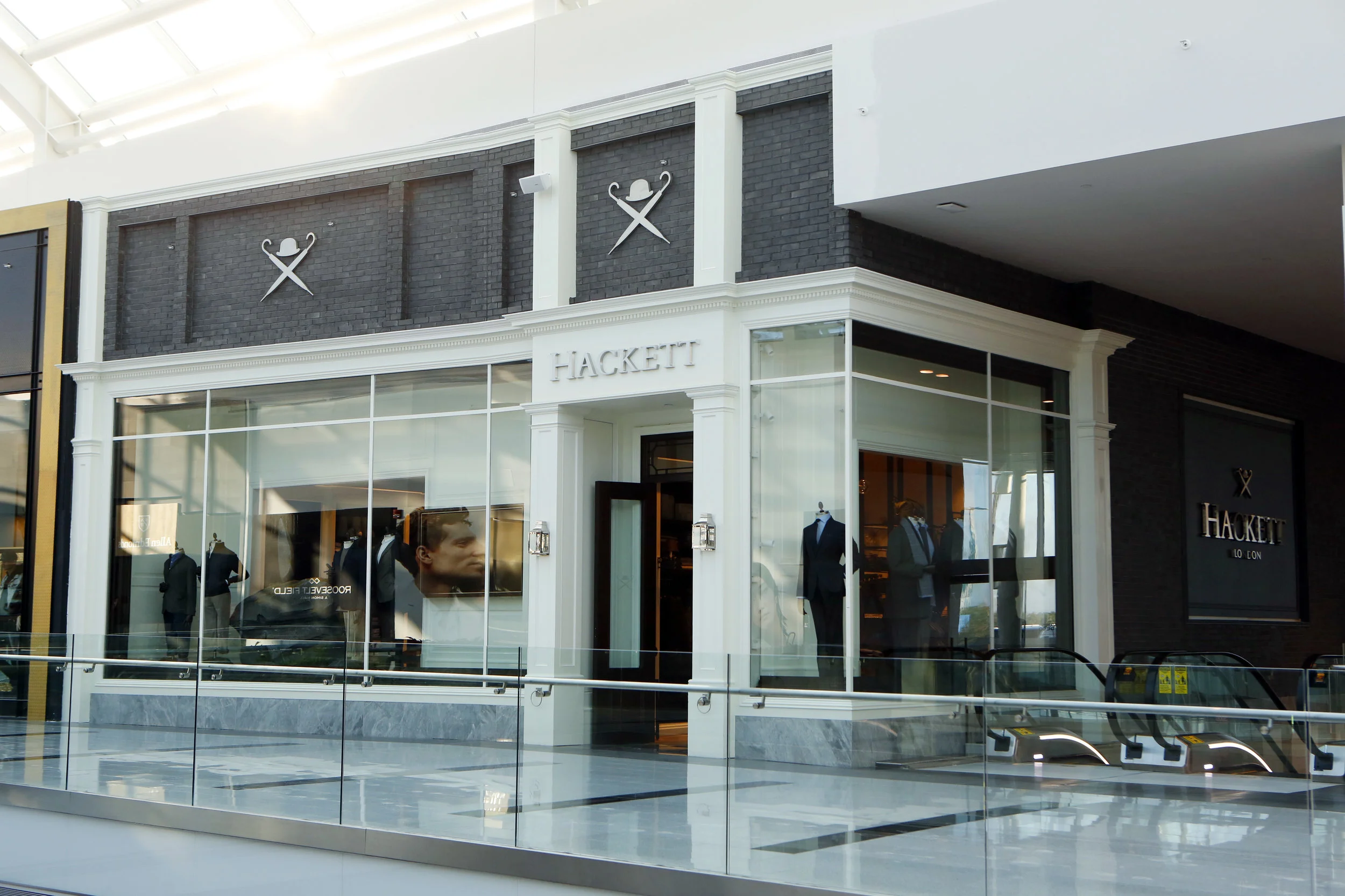 Stylish and chic window display of Hackett London's retail store with the bowler hat and two umbrellas logo over the display. MEP designed by 2L Engineering.