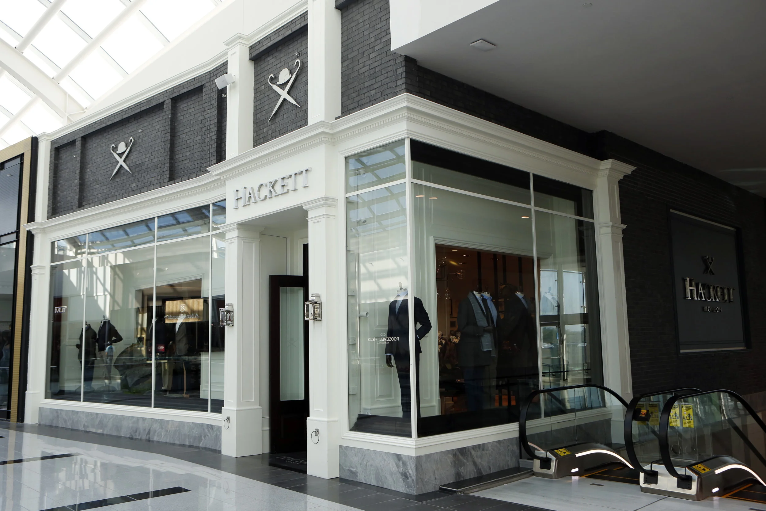 Dark grey brick with the Hackett London logo over the window display and entrance to the British retail store in Woodbury Common Premium Outlet in New York. MEP designed by 2L Engineering