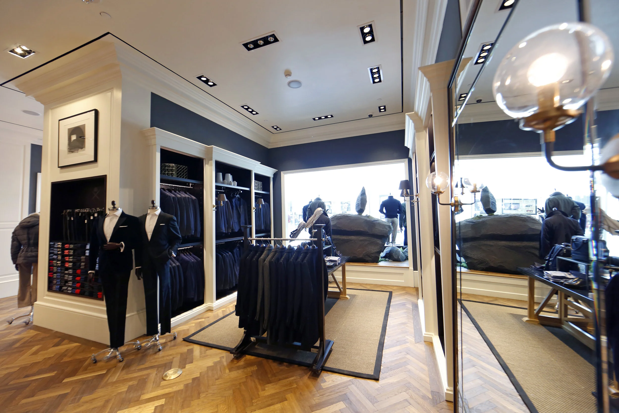 Blazers on display in a retail space with blue accents, and wooden flooring at Hackett London, Woodbury Common Premium outlet. MEP by 2L Engineering.