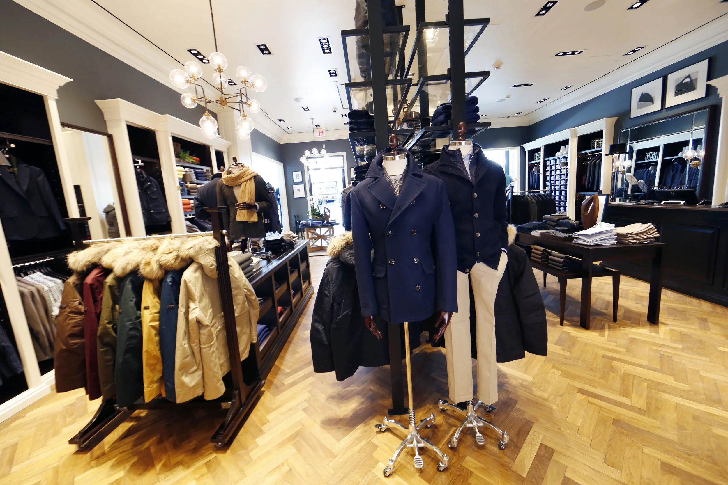 Winter coats on a display rack beside mannequins wearing peacoats in Hackett London, Woodbury Common Premium outlet. MEP designed by 2L Engineering.