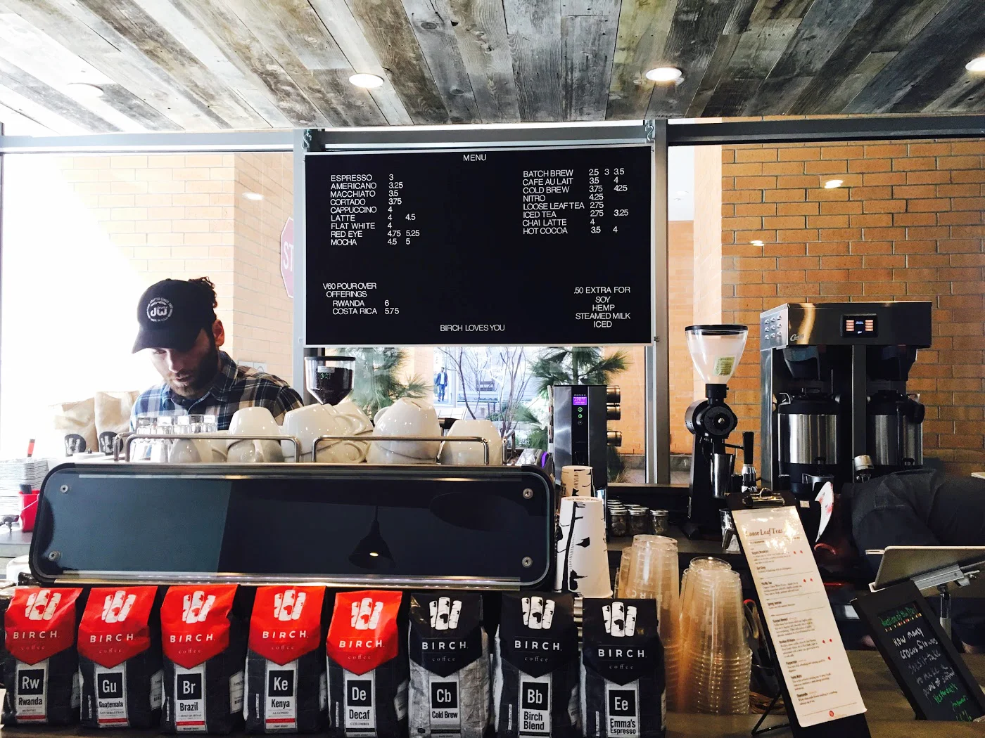 Barista brewing coffee in front of the Birch Coffee menu with Birch Coffee ground coffee on the counter. MEP provided by 2L Engineering.