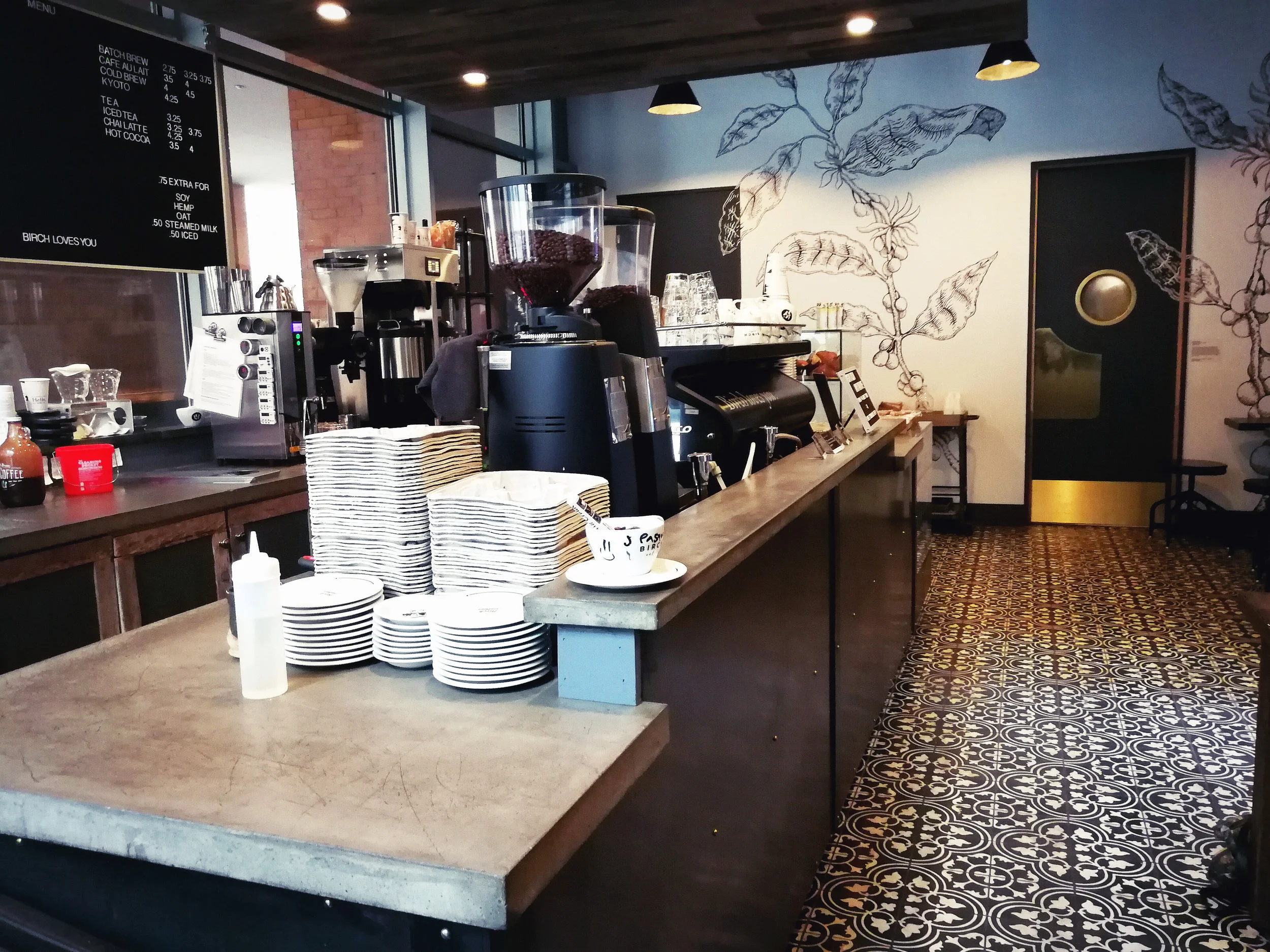 Side view of the Birch Coffee counter with patterned tiles on the floor and plants illustrated on the wall. MEP provided by 2L Engineering.