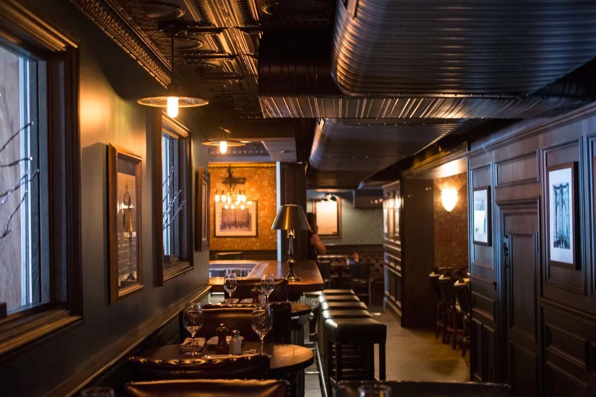Dimly lit room with dark transitional design in the Trading Post, a bar and restaurant in New York's Financial District. MEP provided by 2L Engineering.