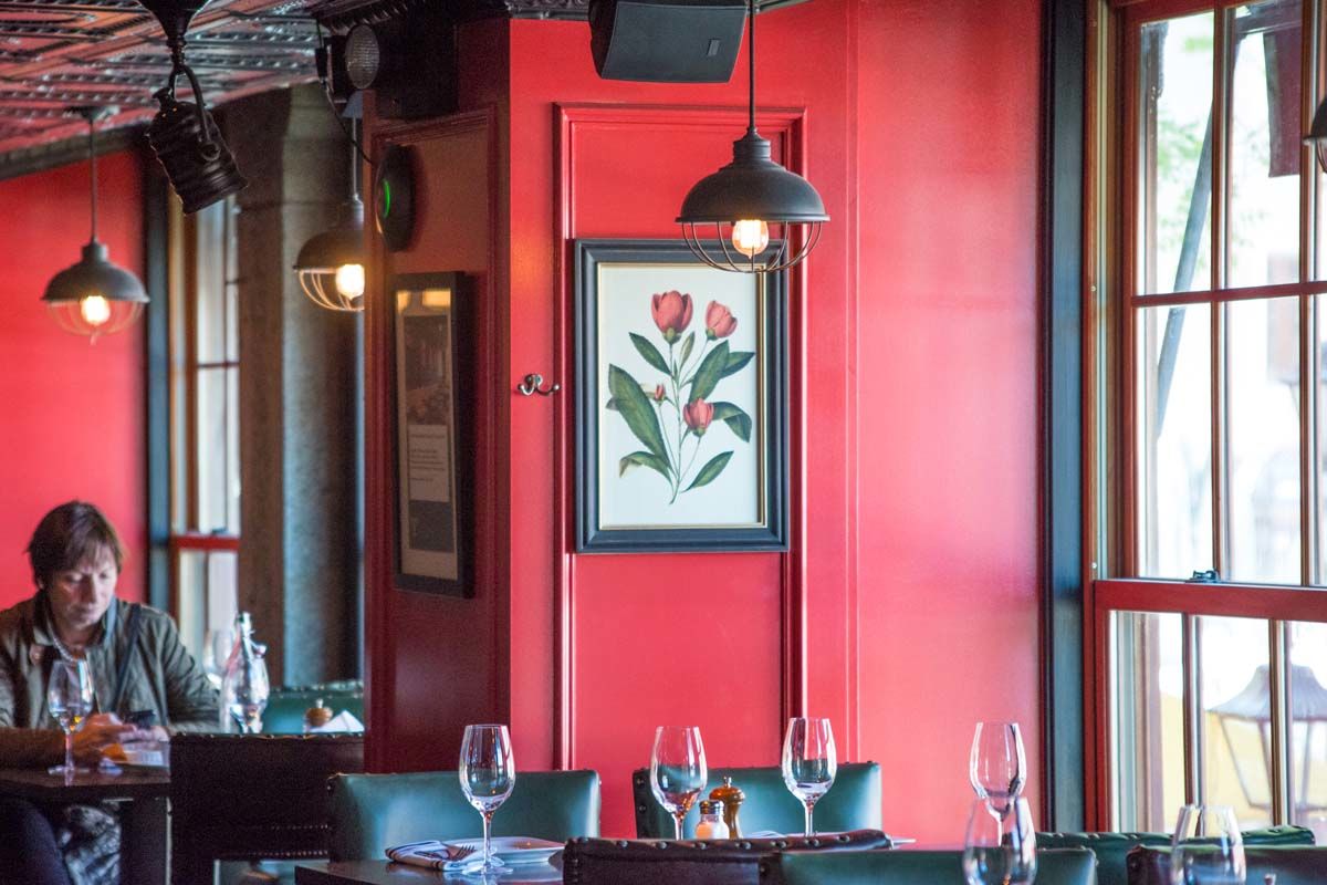 Red painted wall with an illustrated flower on display as a woman enjoys food in the Trading Post, a bar and restaurant located in New York's Financial District. MEP by 2L Engineering.