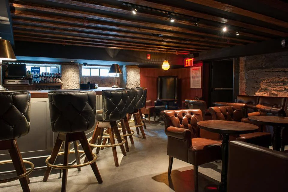 Leather seating throughout a room and by a bar in the basement of the Trading Post, a bar and restaurant in New York's Financial District. MEP provided by 2L Engineering.