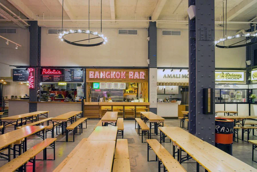Food hall with wood bench seating in Urbanspace Vanderbilt with the view facing Bangkok Bar, Robusta's Pizza and other eateries. MEP designed by 2L Engineering.