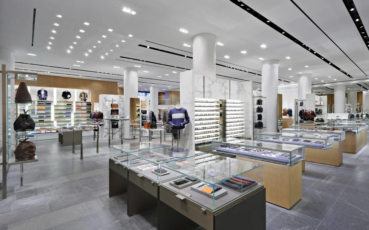 Wallet, sunglasses, and bag displays with menswear in the background at Barney's New York. MEP designed by 2L Engineering.