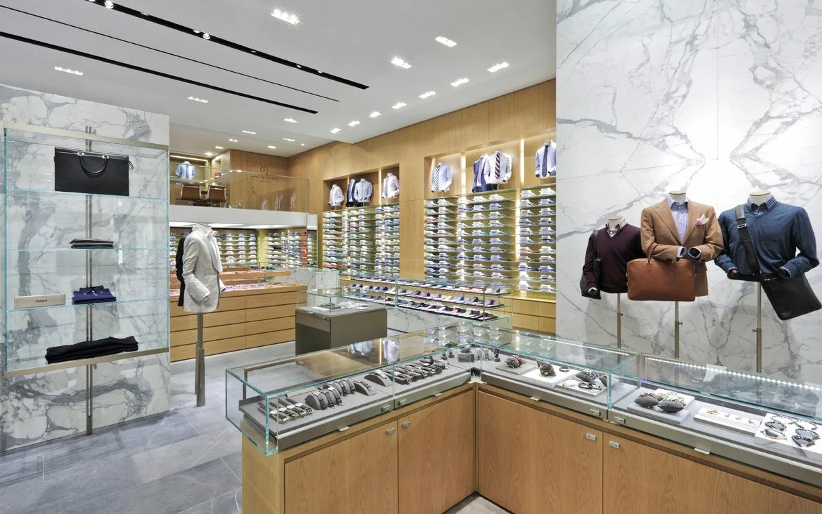 Watches in a display case with mannequins wearing smartly dressed clothes and leather goods in Barney's New York. MEP designed by 2L Engineering.