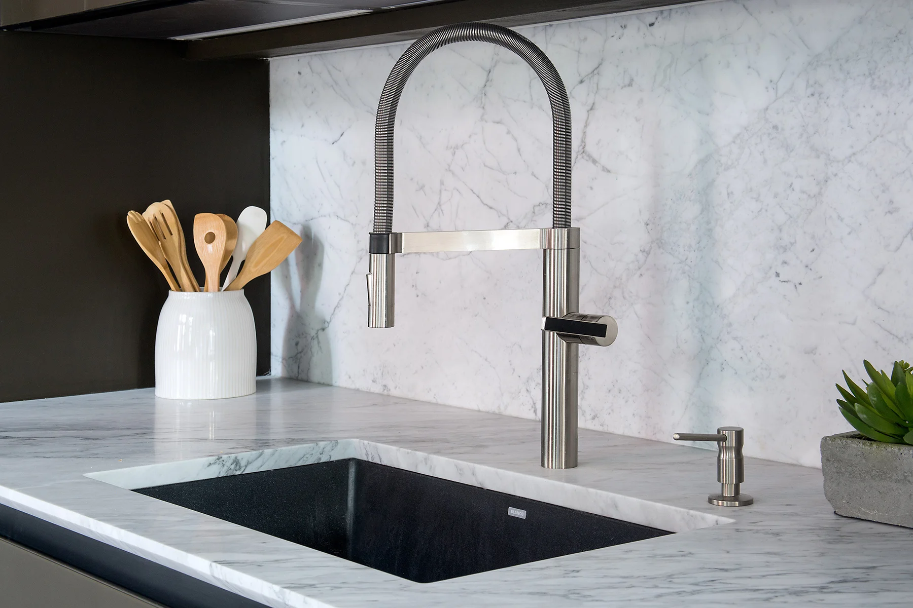 Detail shot of a minimalistic kitchen sink with marble detailing on the counter and wall and a plant. MEP designed by 2L Engineering.