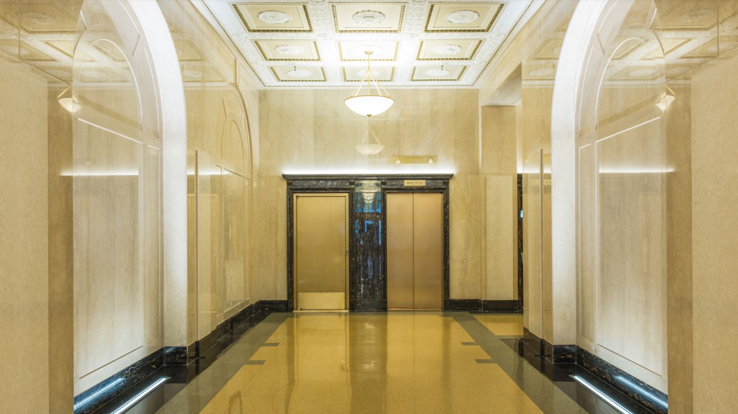 Gold elevators in a brightly lit lobby featuring a chandelier and delicate, flowery ceiling moldings. MEP design provided by 2L Engineering. 