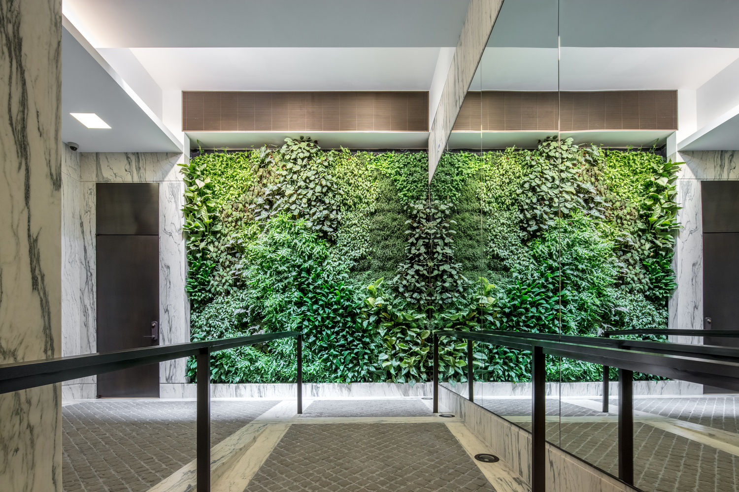 Front view of a brightly lit living green wall with tiled and marble flooring and a mirror facing the elevators. MEP provided by 2L Engineering.
