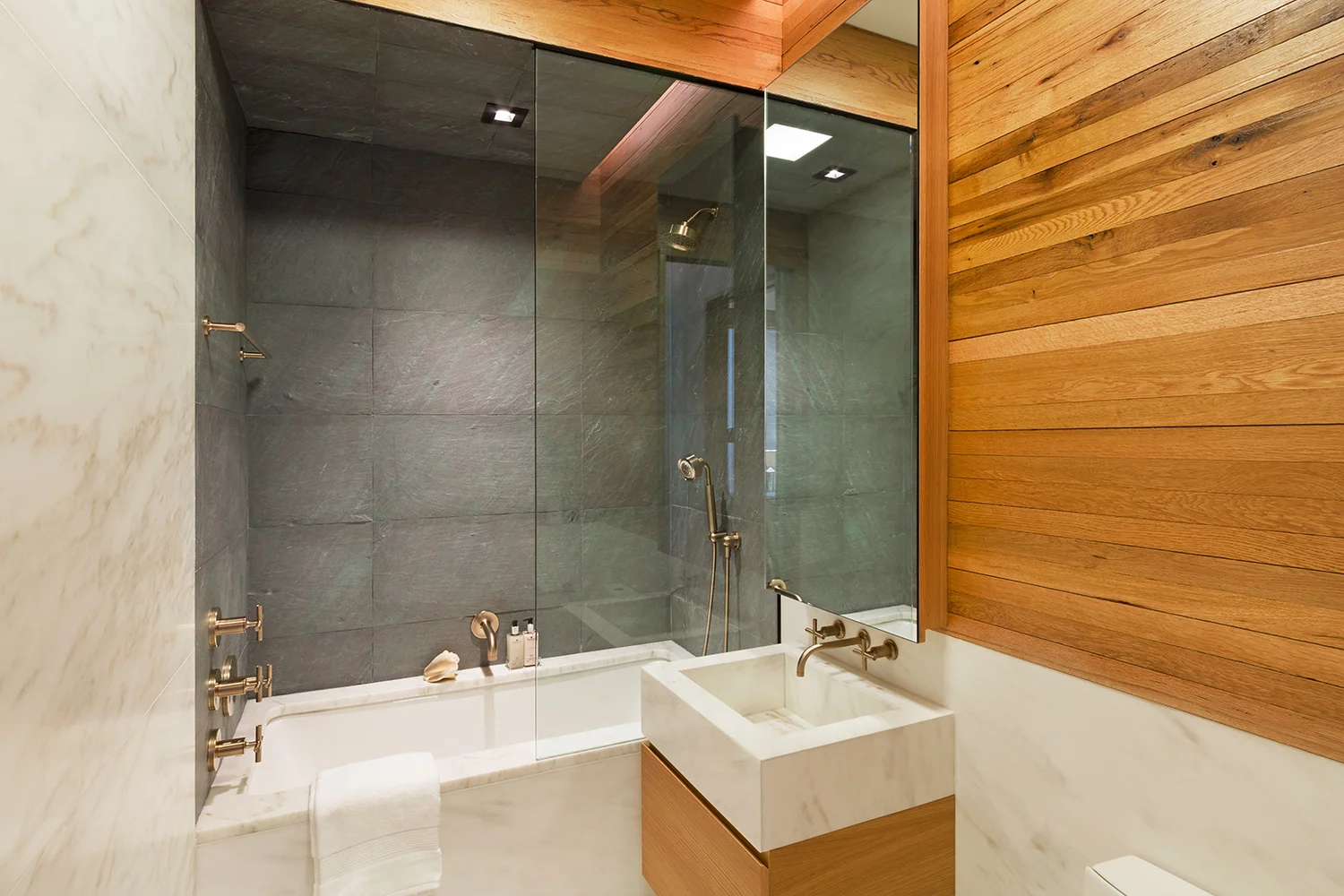 Wood paneled walls in a luxury bathroom featuring a bathtub and shower combo. MEP provided by 2L Engineering.