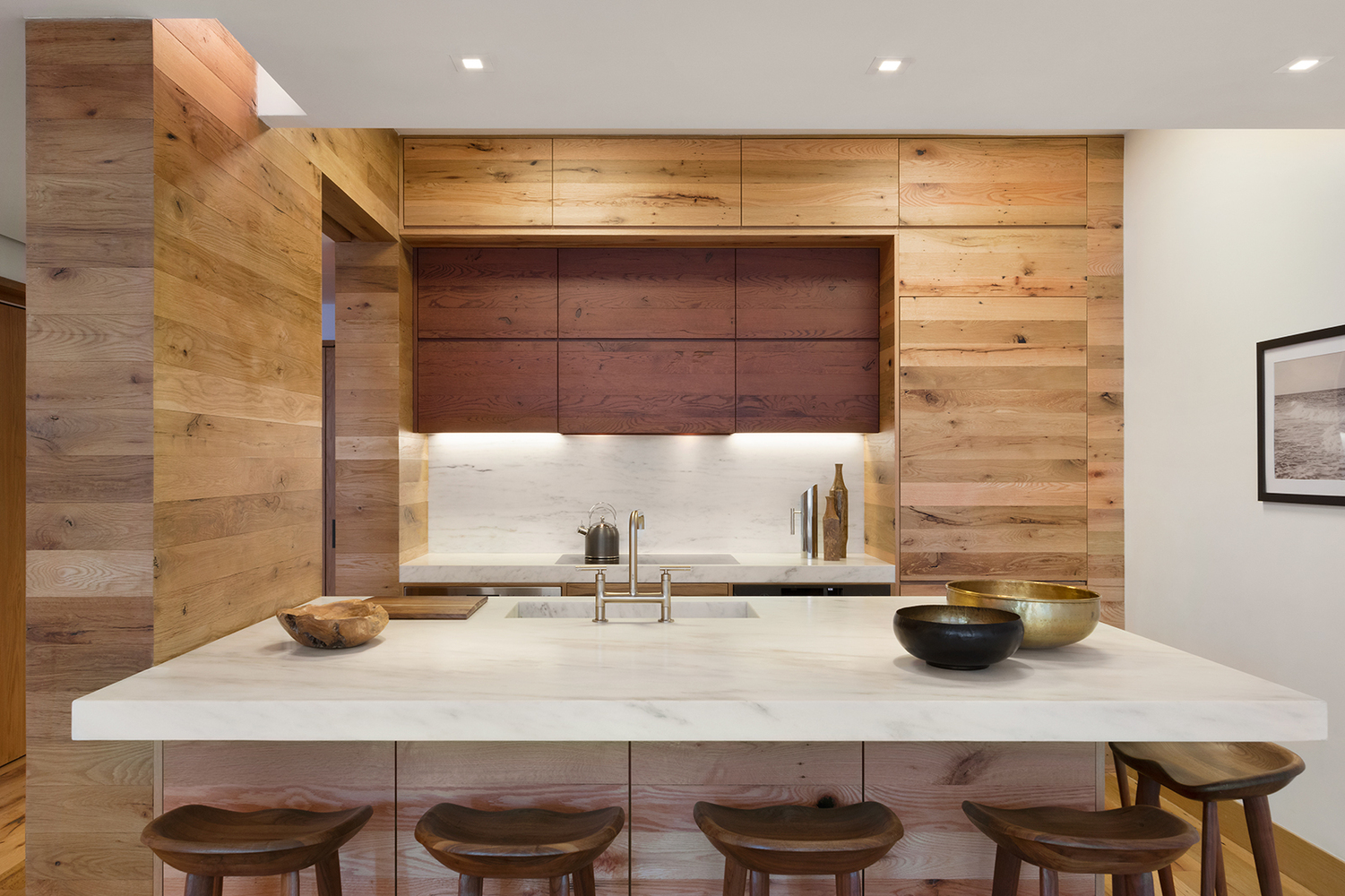 Wood paneled storage spaces in a rustic kitchen with marble counters and a teapot on the stove. MEP designed by 2L Engineering.