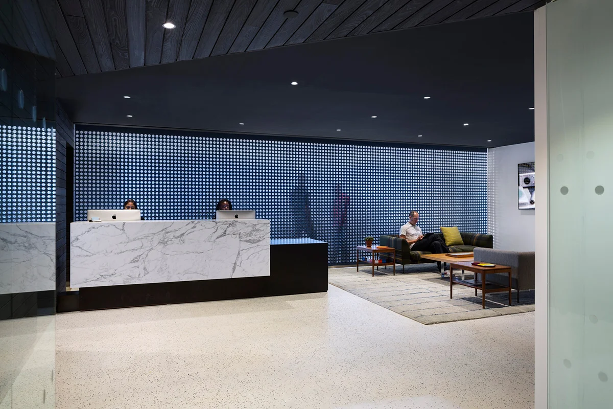 A backlit reception and lounge area with a geometric wall in the offices of Droga 5. MEP provided by 2L Engineering.