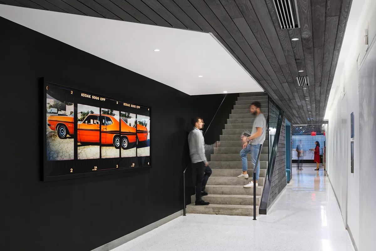 Two men having a conversation on the stairs beside artwork of an orange car in the offices of Droga5. MEP Provided by 2L Engineering.
