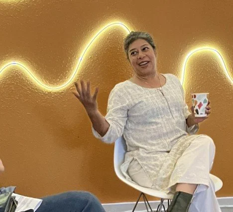 A person in white seated in front of a light sculpture against a golden-brown wall.