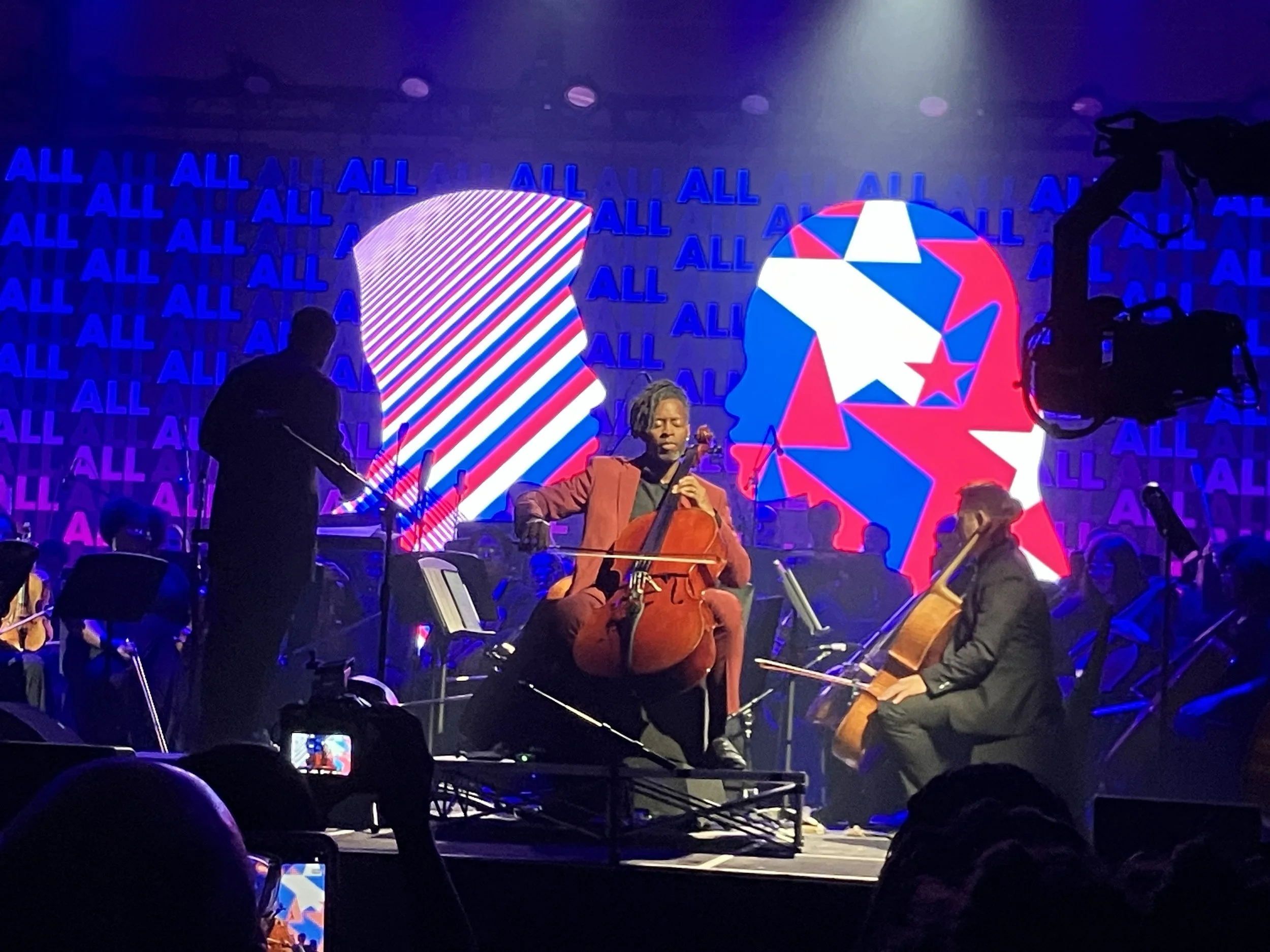 An orchestra plays on stage with red, white, and blue scenery