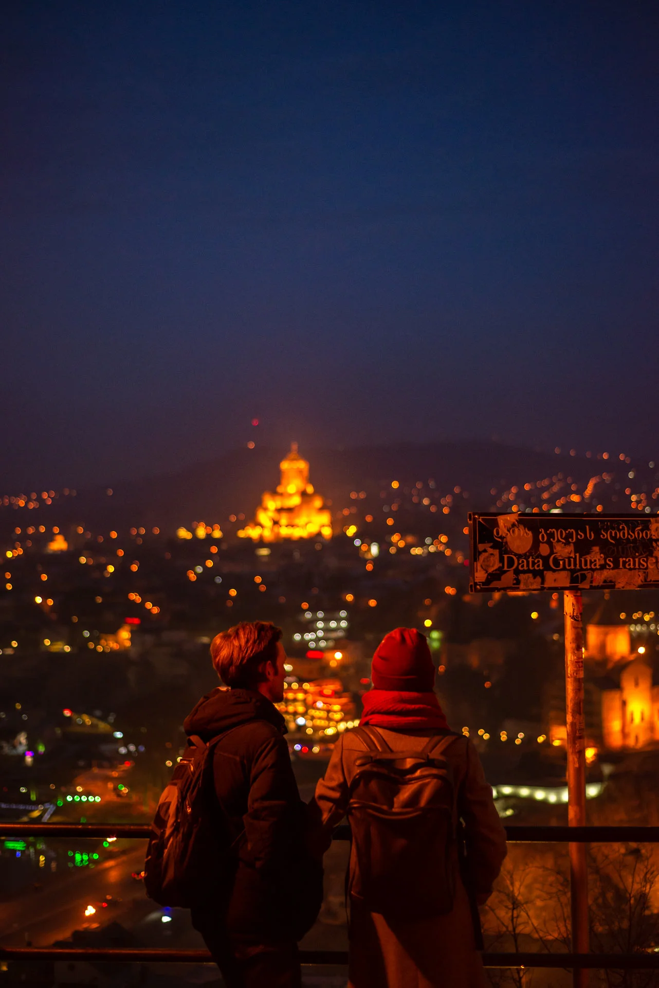 A young couple enjoying Tbilisi by night from a nearby hill.