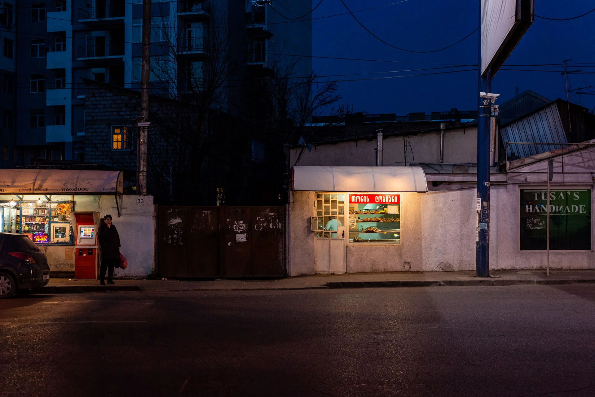 A woman looking curiously at the camera next to a late-night pastry shop.