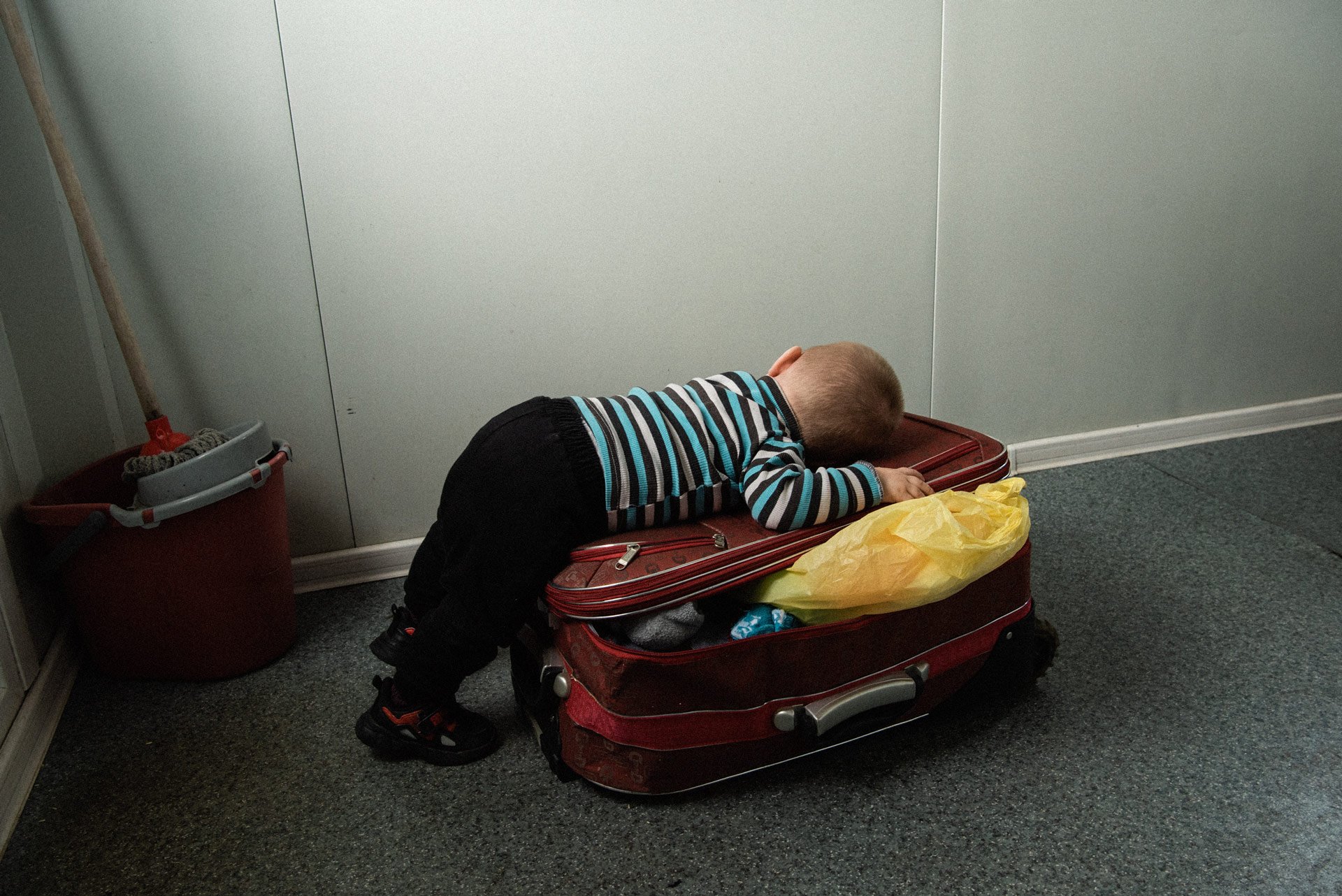 A Ukrainian refugee kid resting on his mother’s suitcase.