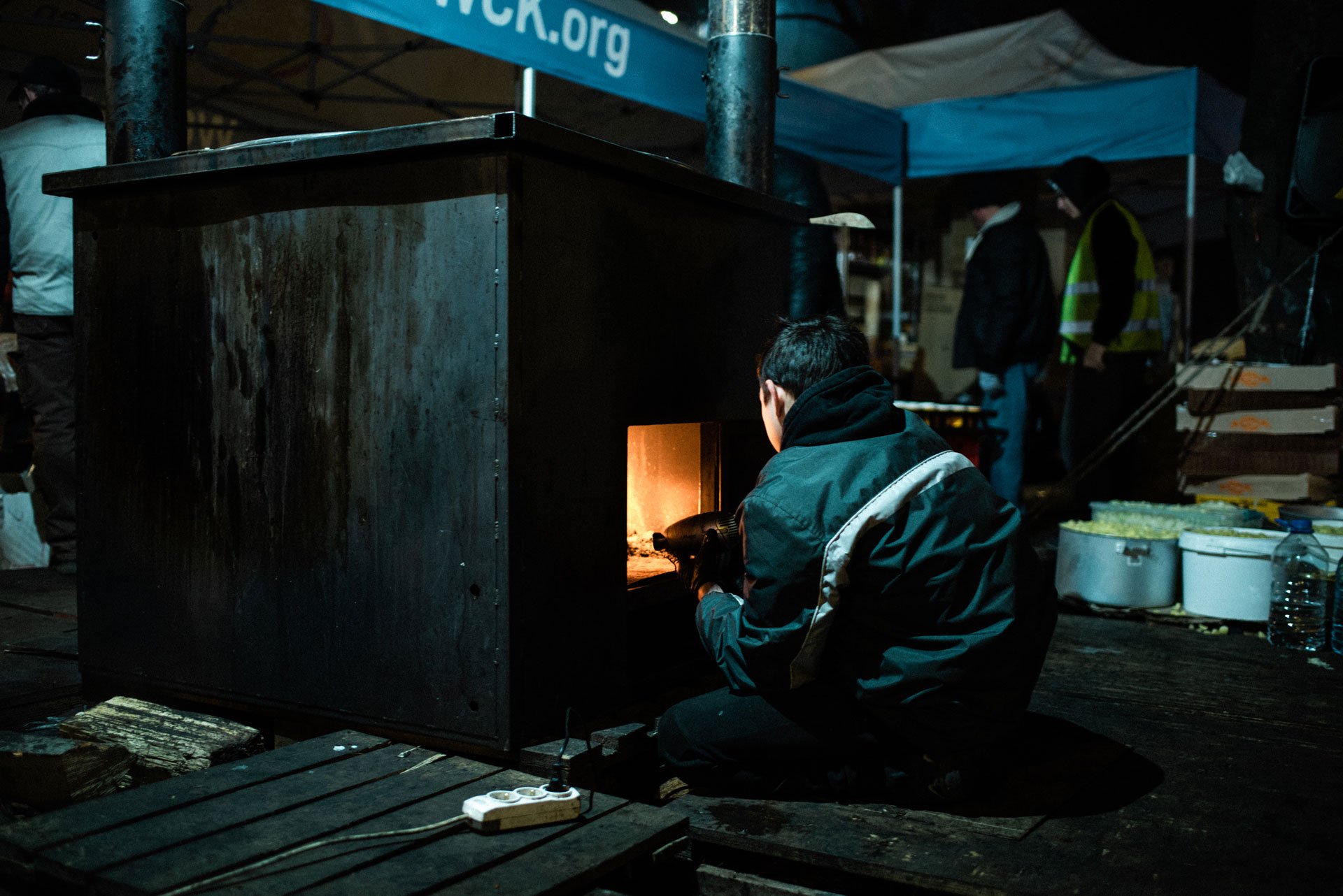 A boy looks after the fire of a metal stove and warms up his hands at the plaza outside Lviv’s train station.