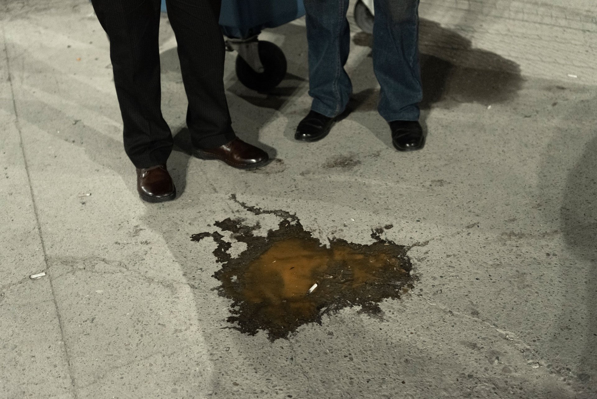 Two men looking over a pool of spilled drinks and cigarette buds.