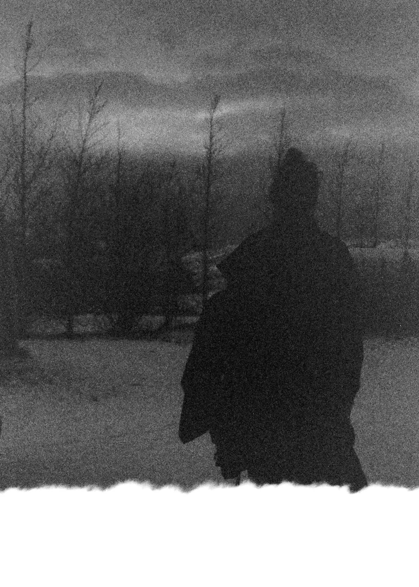 A silhouette of a person standing outdoors in a snowy landscape with bare trees and dark clouds in the sky.