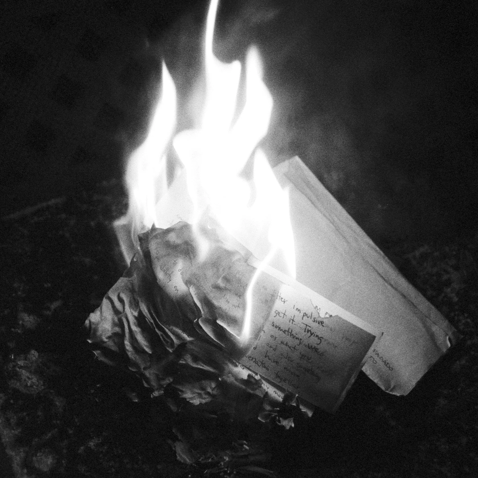 A piece of paper on fire, burning and crumpled at one end, with handwritten notes visible on the paper.