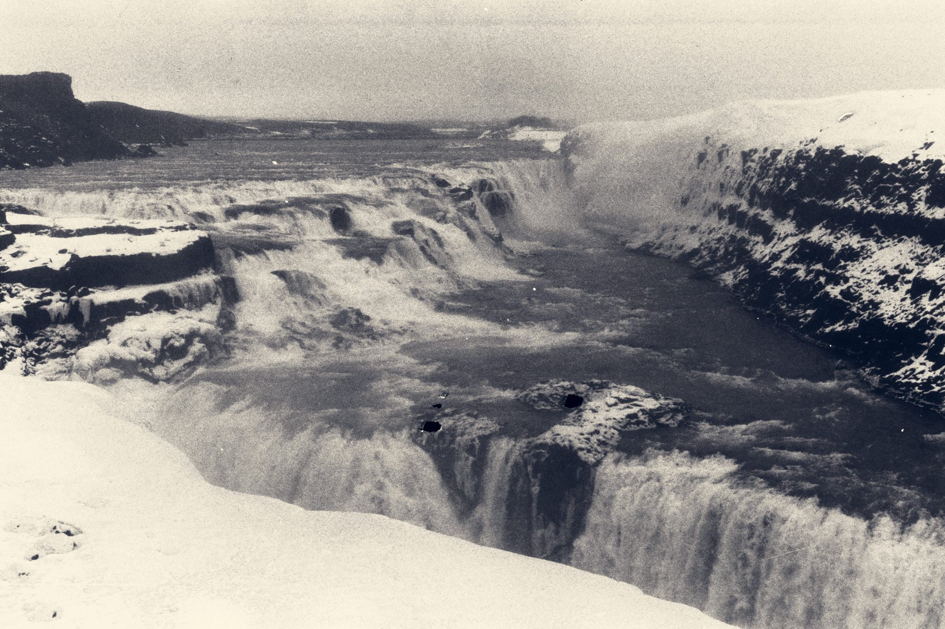 Black and white photo of Gullfoss waterfall in Iceland, surrounded by snow and rocky cliffs.