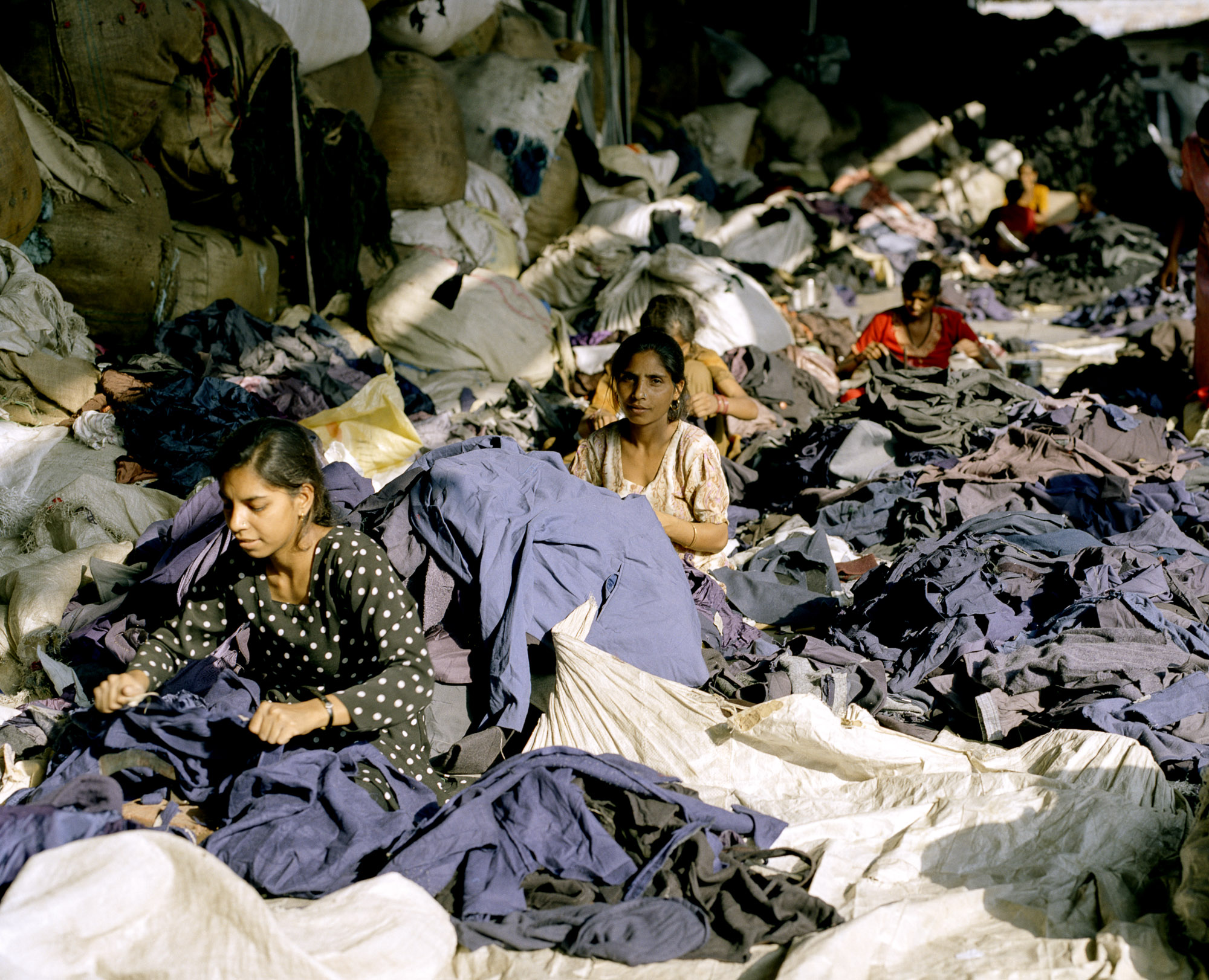 Women cut up jumpers, jackets and coats using traditional vegetable cutters. Garment labels advertising expensive brand names and global origins are discarded as worthless information.