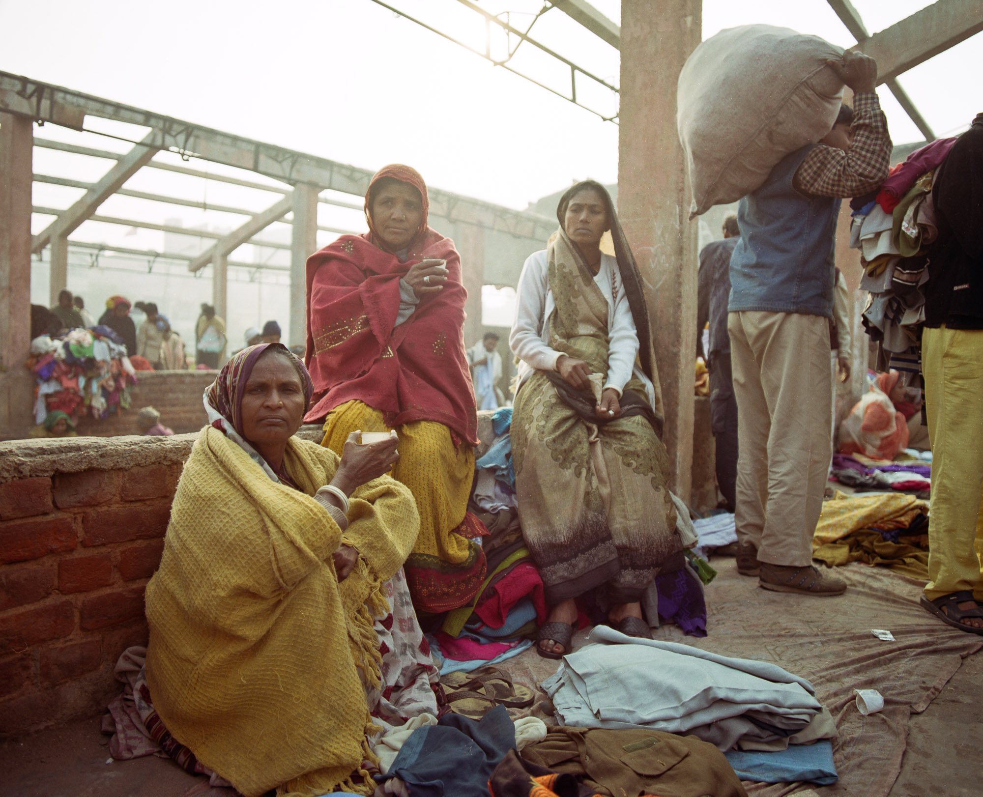  Women drinking chai on a December morning. Families often work together, traveling to their regular suburban patches to barter for clothes and selling them together at the market. 