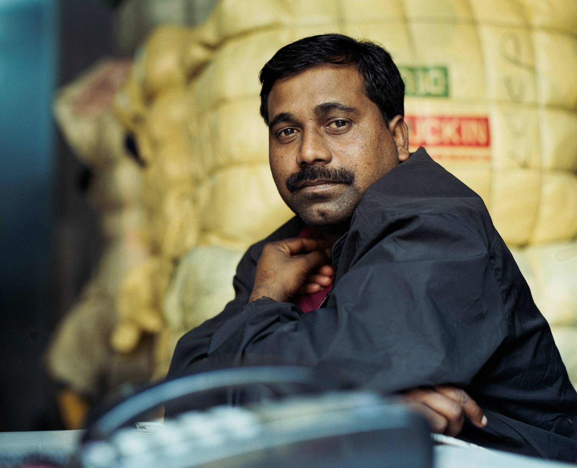 Bales of exported western clothing sit behind a dealer in global second-hand garments in Azad Market, Old Delhi.
