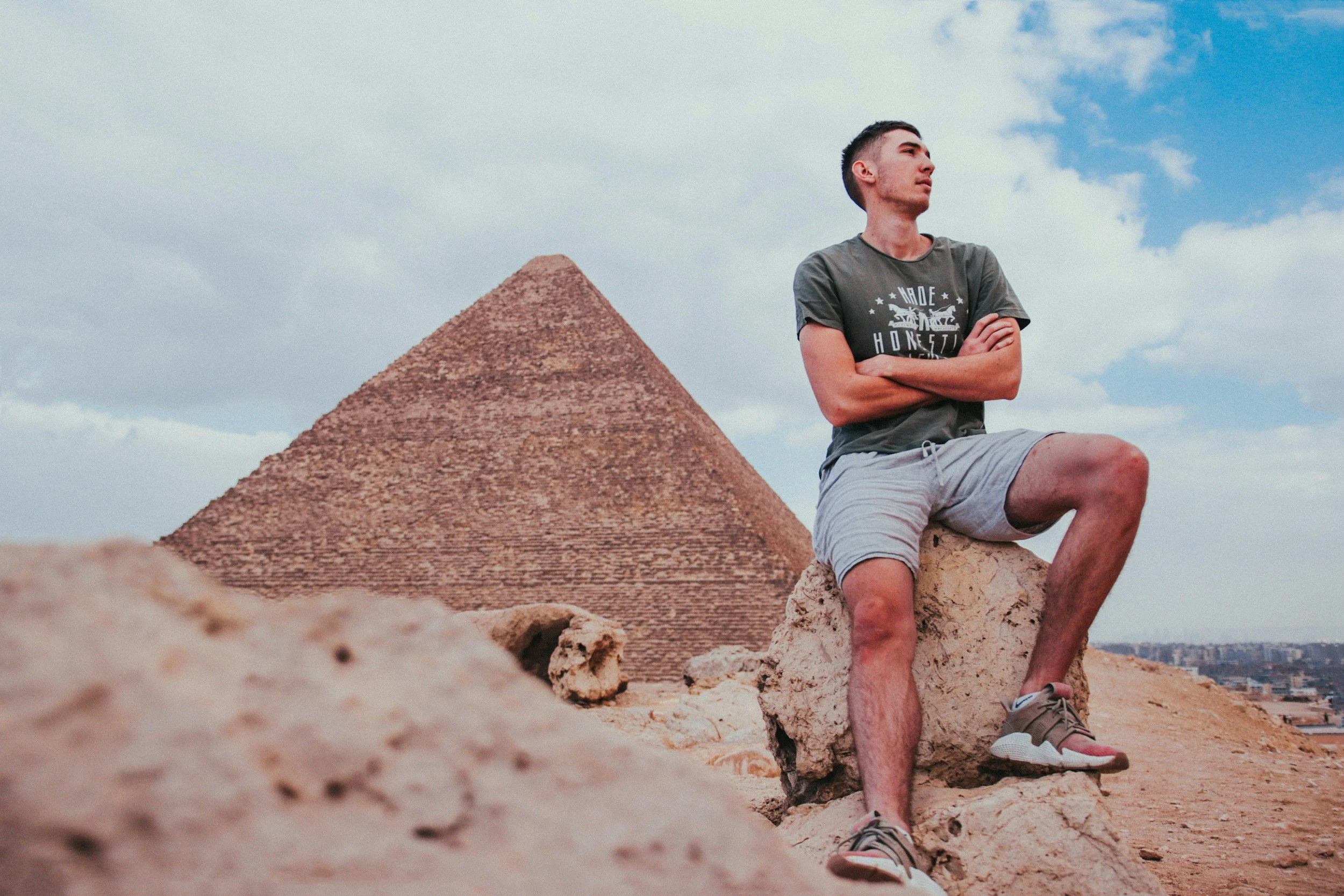 young man sitting on rock at the base of a pyramid