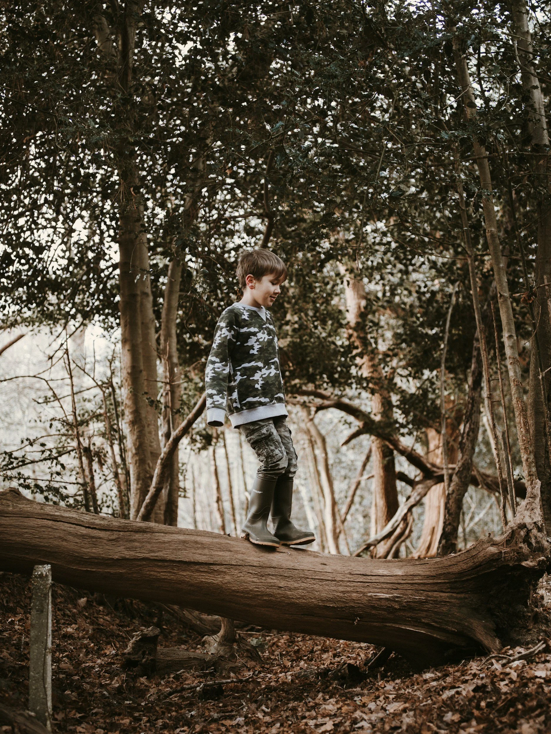 A boy balancing and walking across a log in the woods