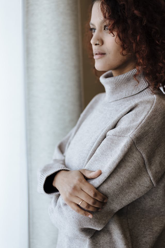 woman standing by window with arms crossed with reflective expression