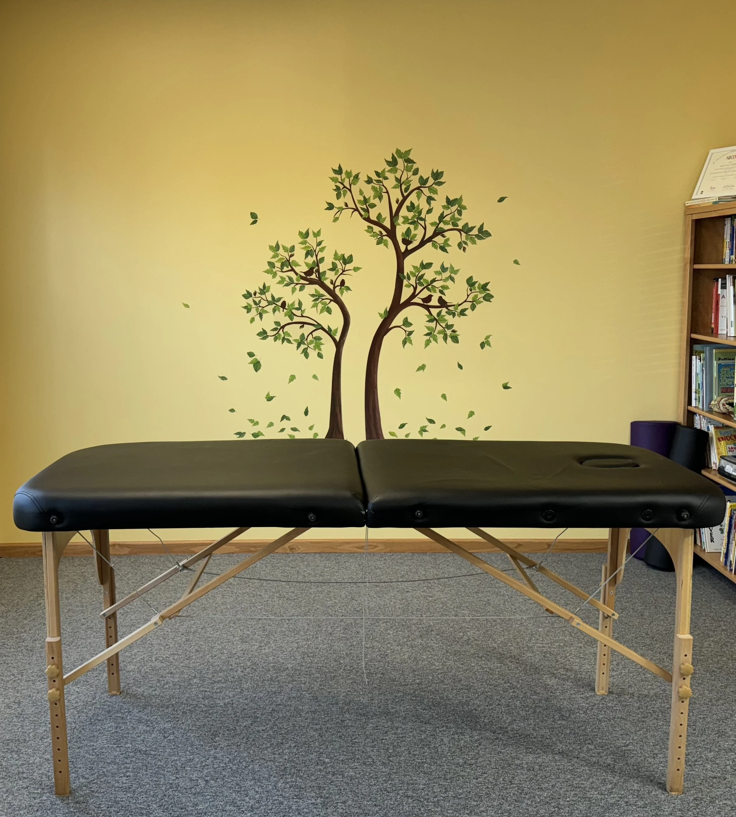 a massage table set up against a yellow wall with trees painted on it