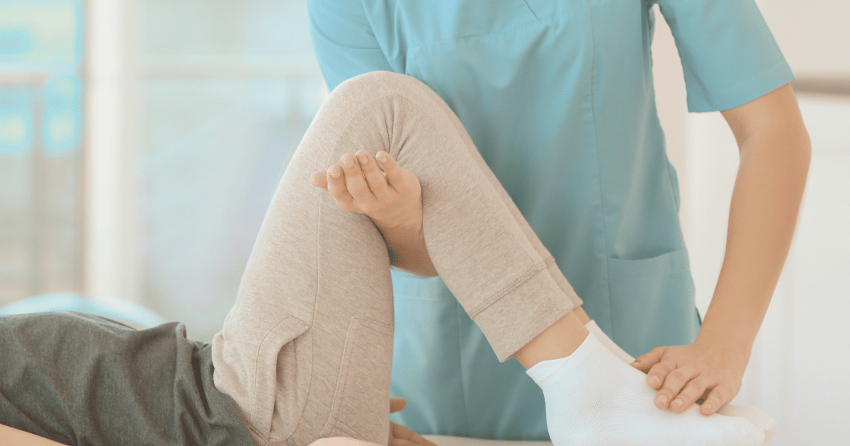 child with bent knees while therapist helps