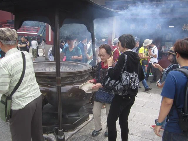 A woman leaves an incense brazier partway between the entry gate and the main steps up to the temple. Copyright 2017, Anna Broadway.