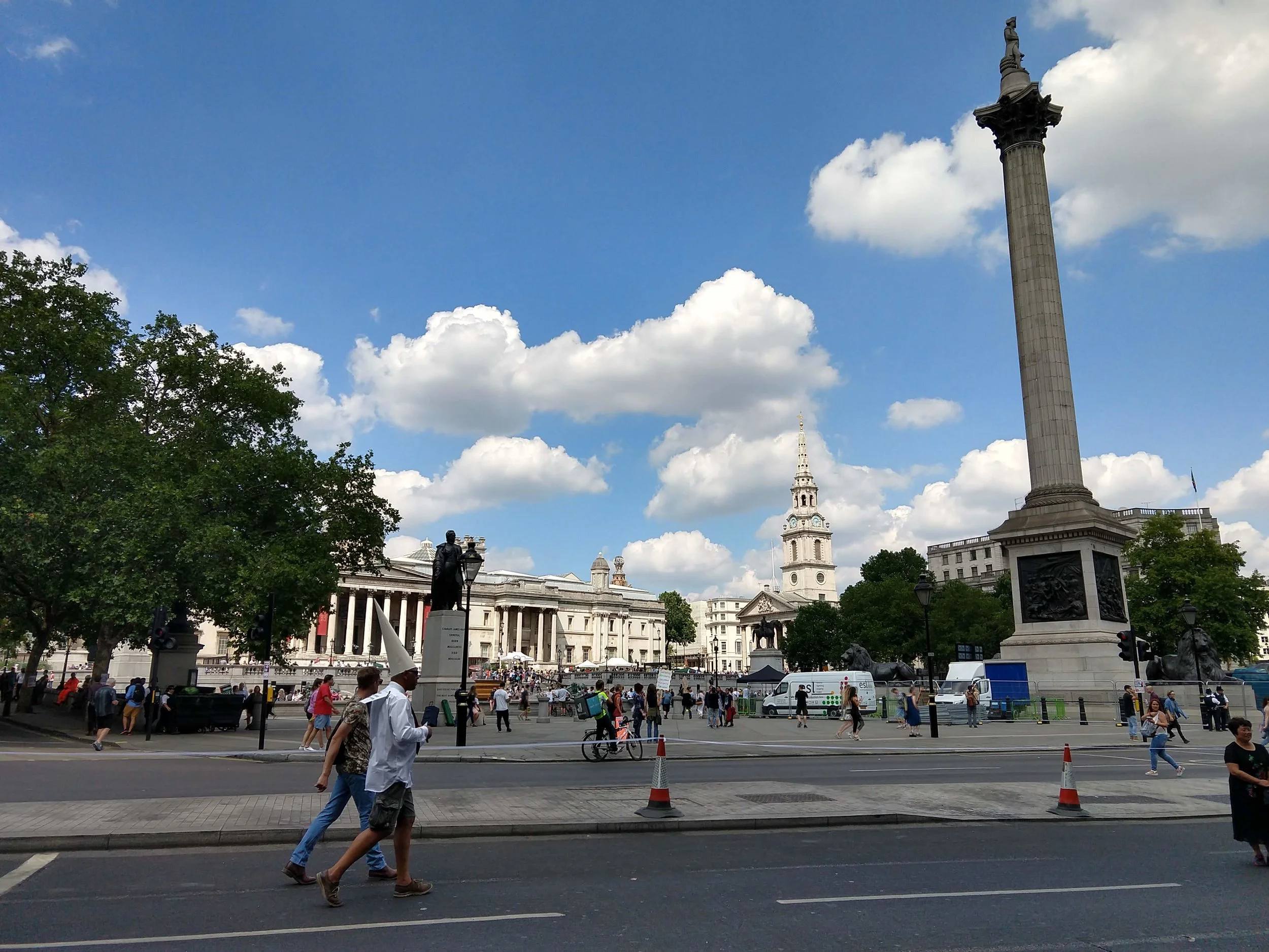A man in a dunce cap walks past Trafalgar Square.