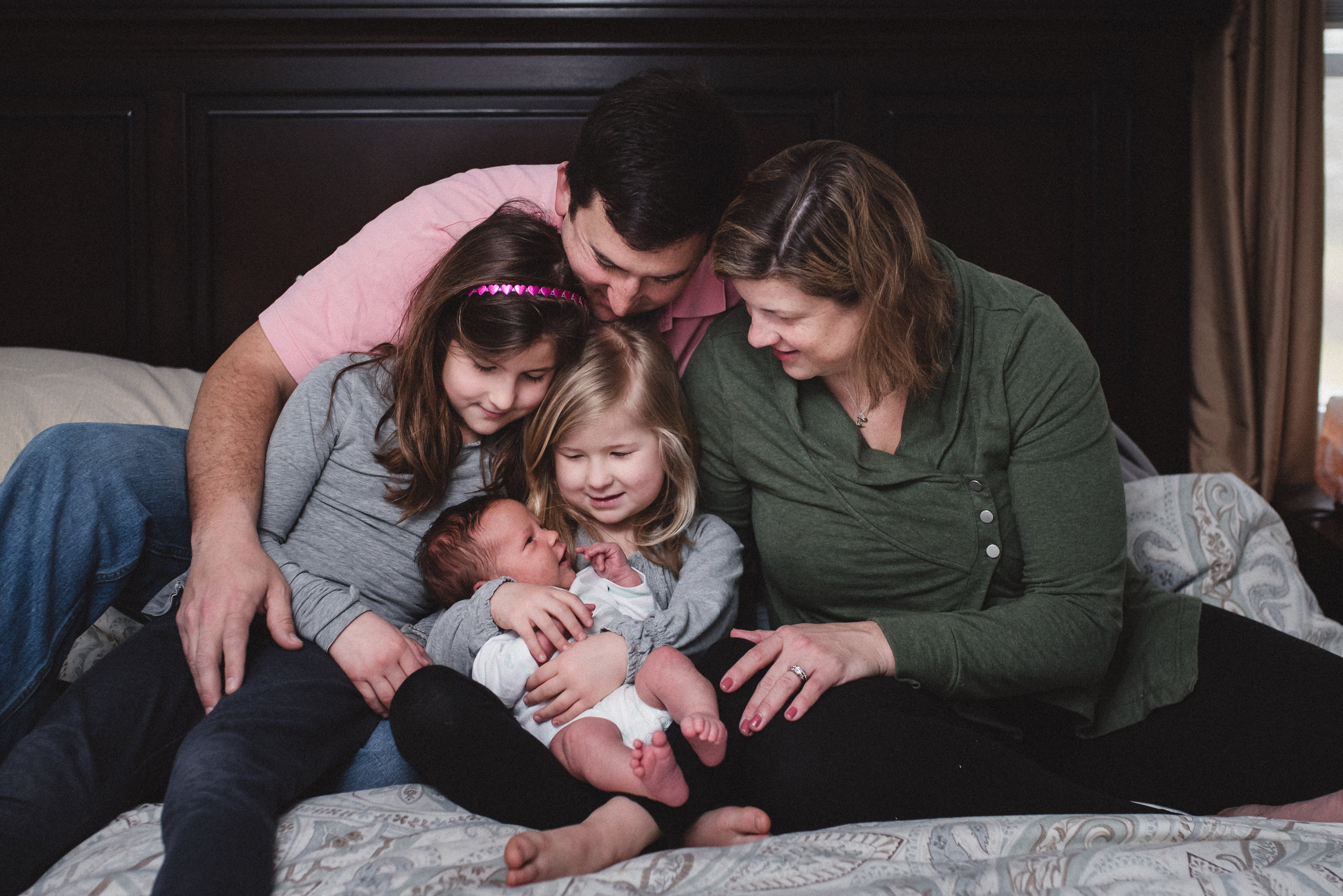 family sitting on bed holding newborn baby 