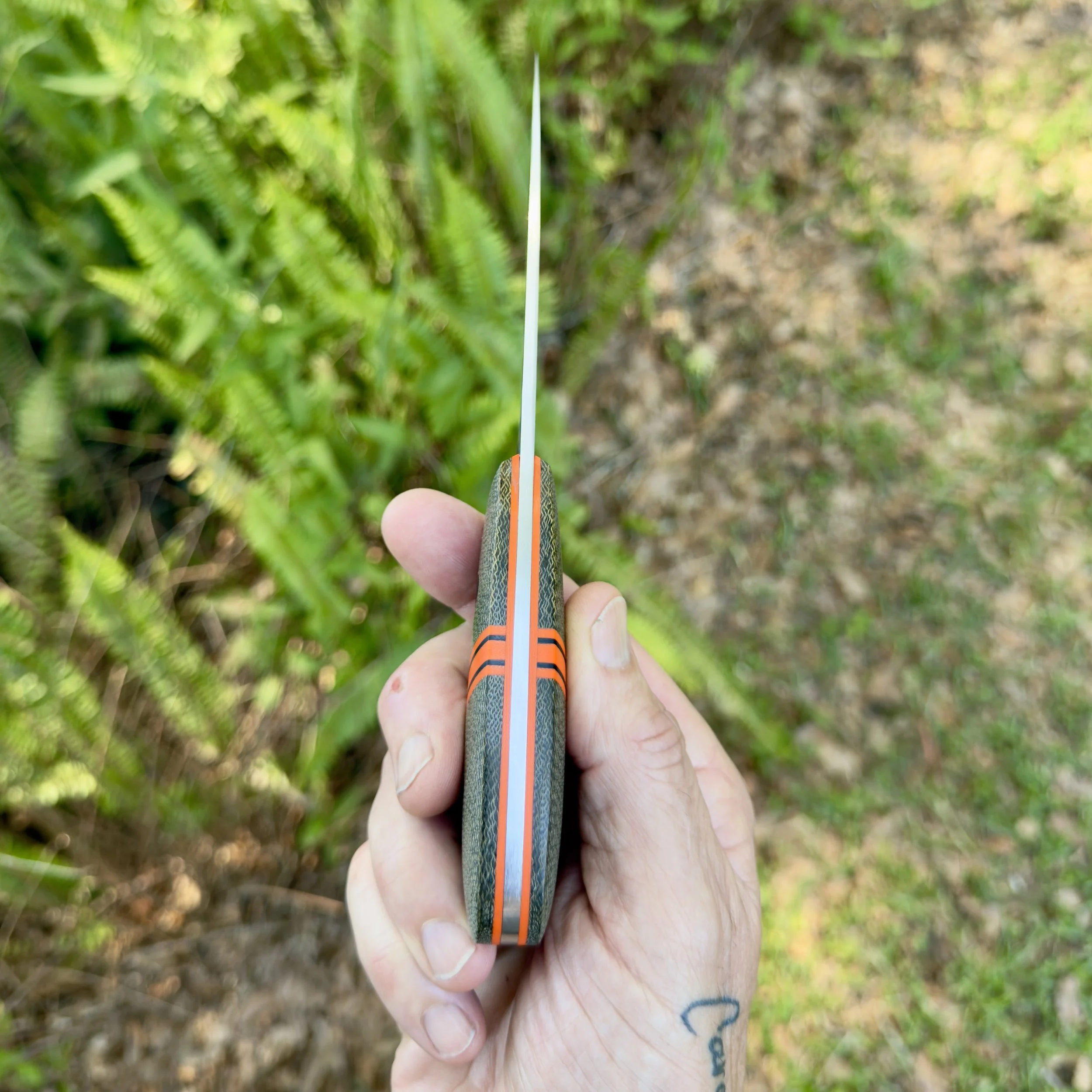 Spine view of handmade EDC knife showing blade thickness and orange G10 liners on green micarta handle