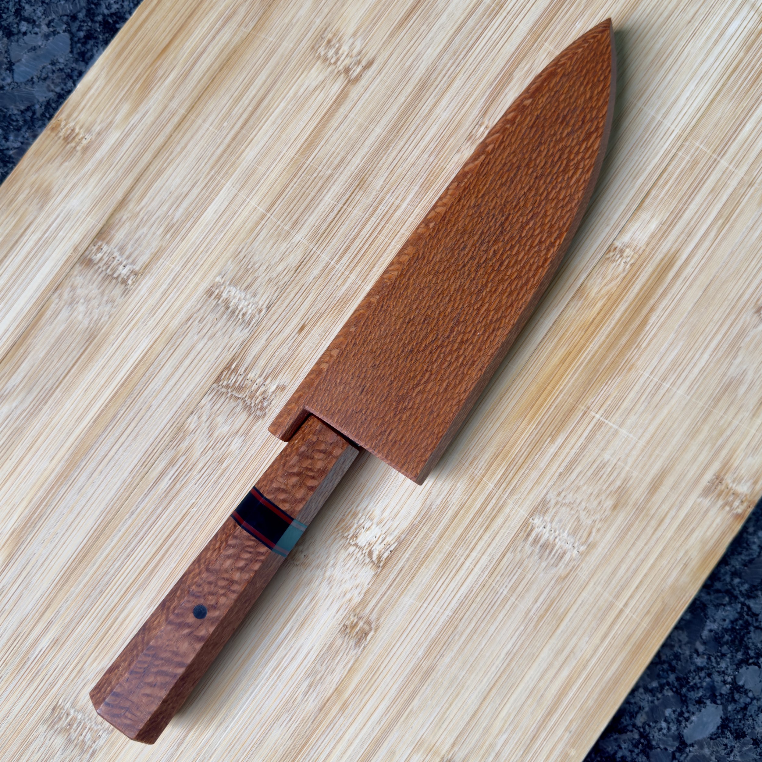 Petty knife in lacewood saya with matching lacewood handle resting on wooden cutting board
