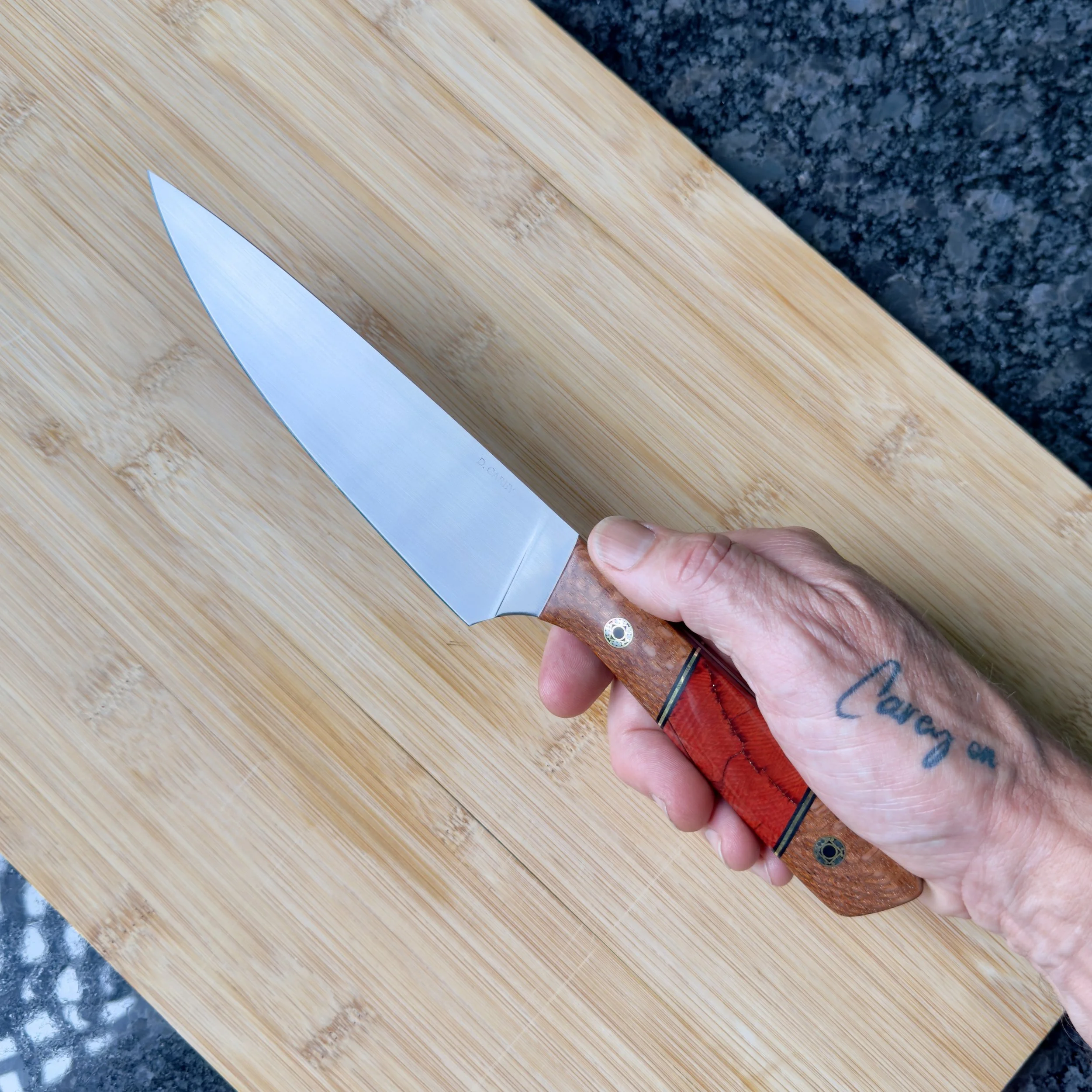 52100 carbon steel chef knife with lacewood and mammoth tusk handle held in hand